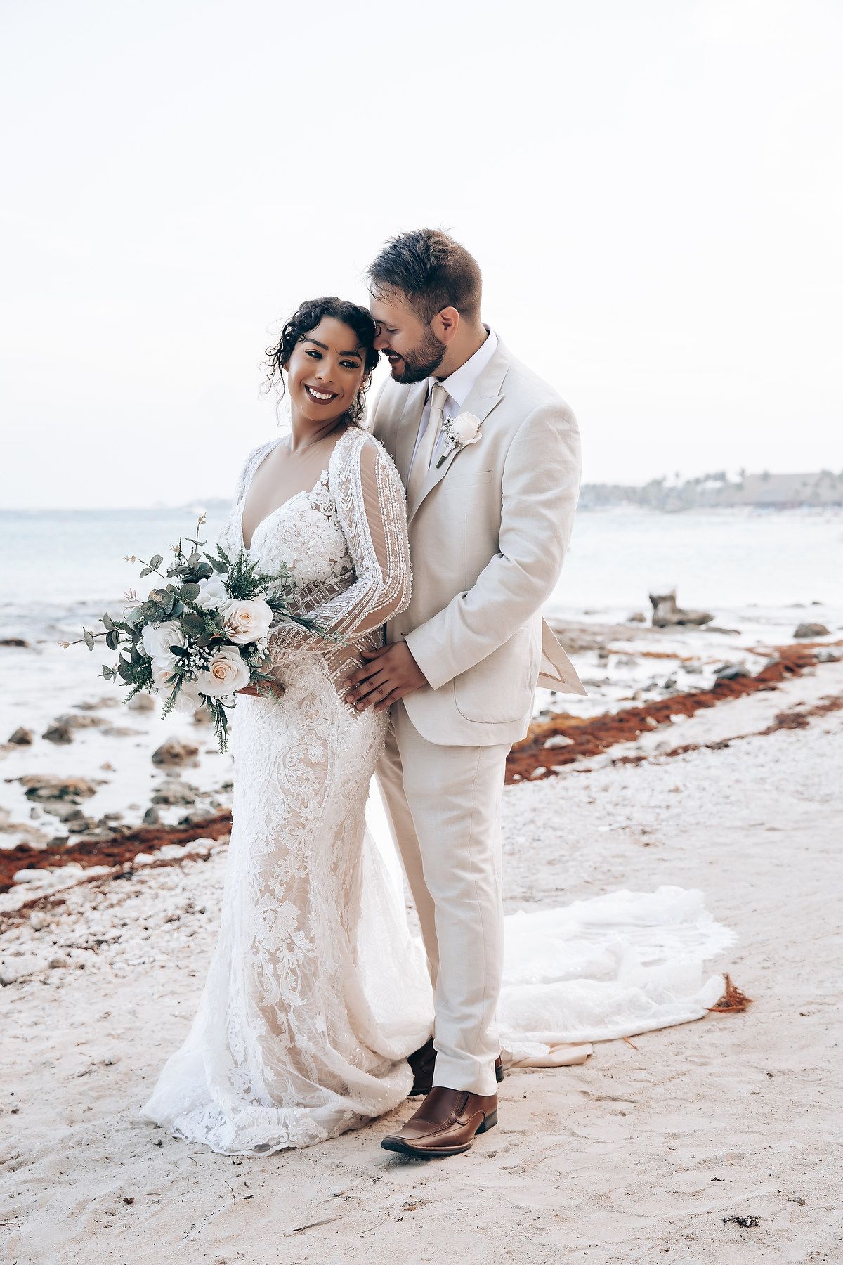Romantic beach wedding photos featuring a lace dress and white suit on a sandy shoreline.