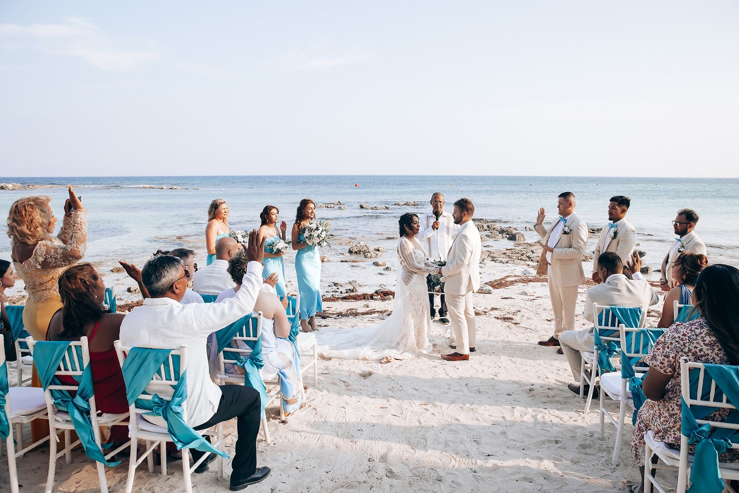 Beachside wedding ceremony setup with turquoise chairs and white decor overlooking the ocean.