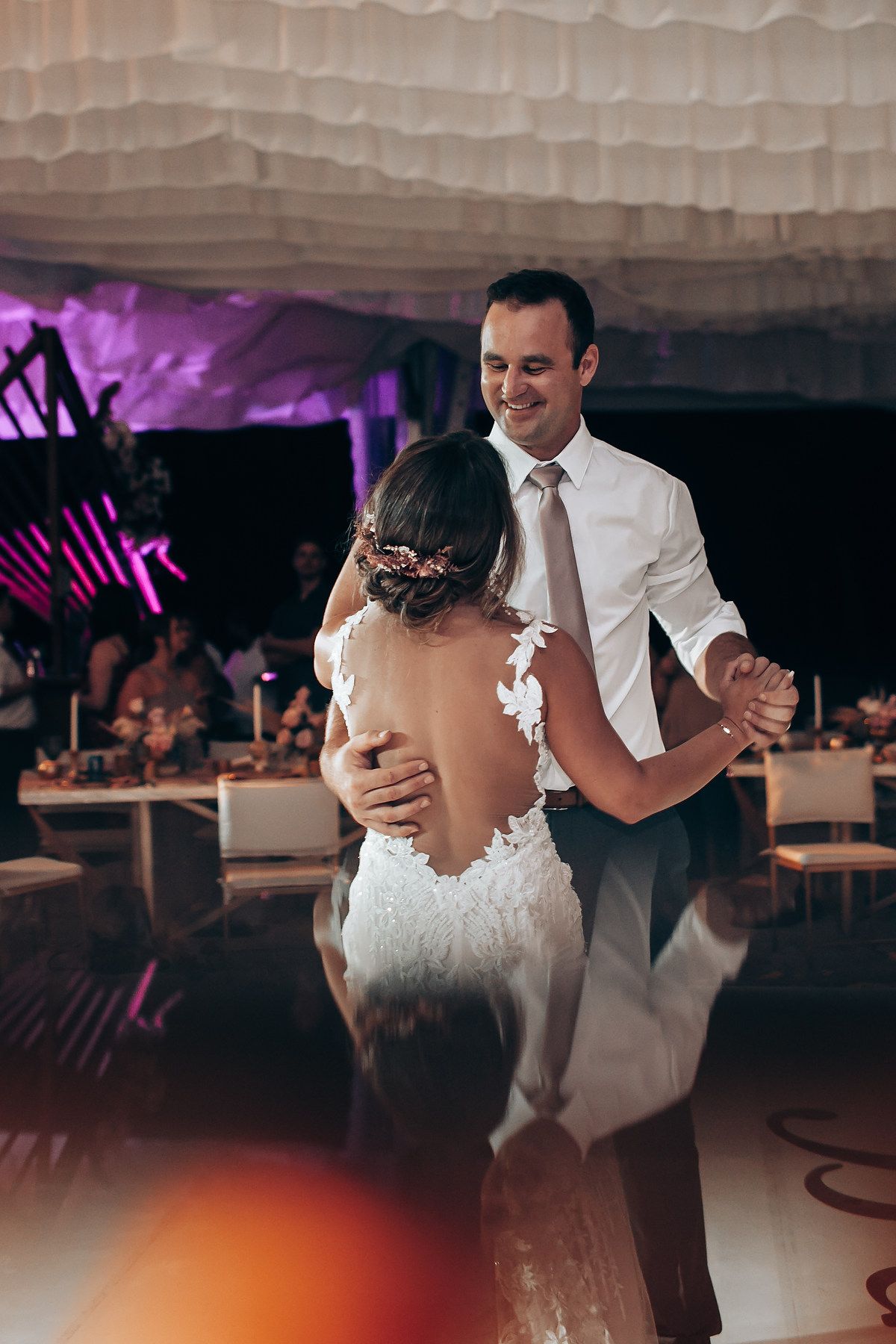 Romantic first dance at wedding reception under soft white draping and purple ambient lighting.