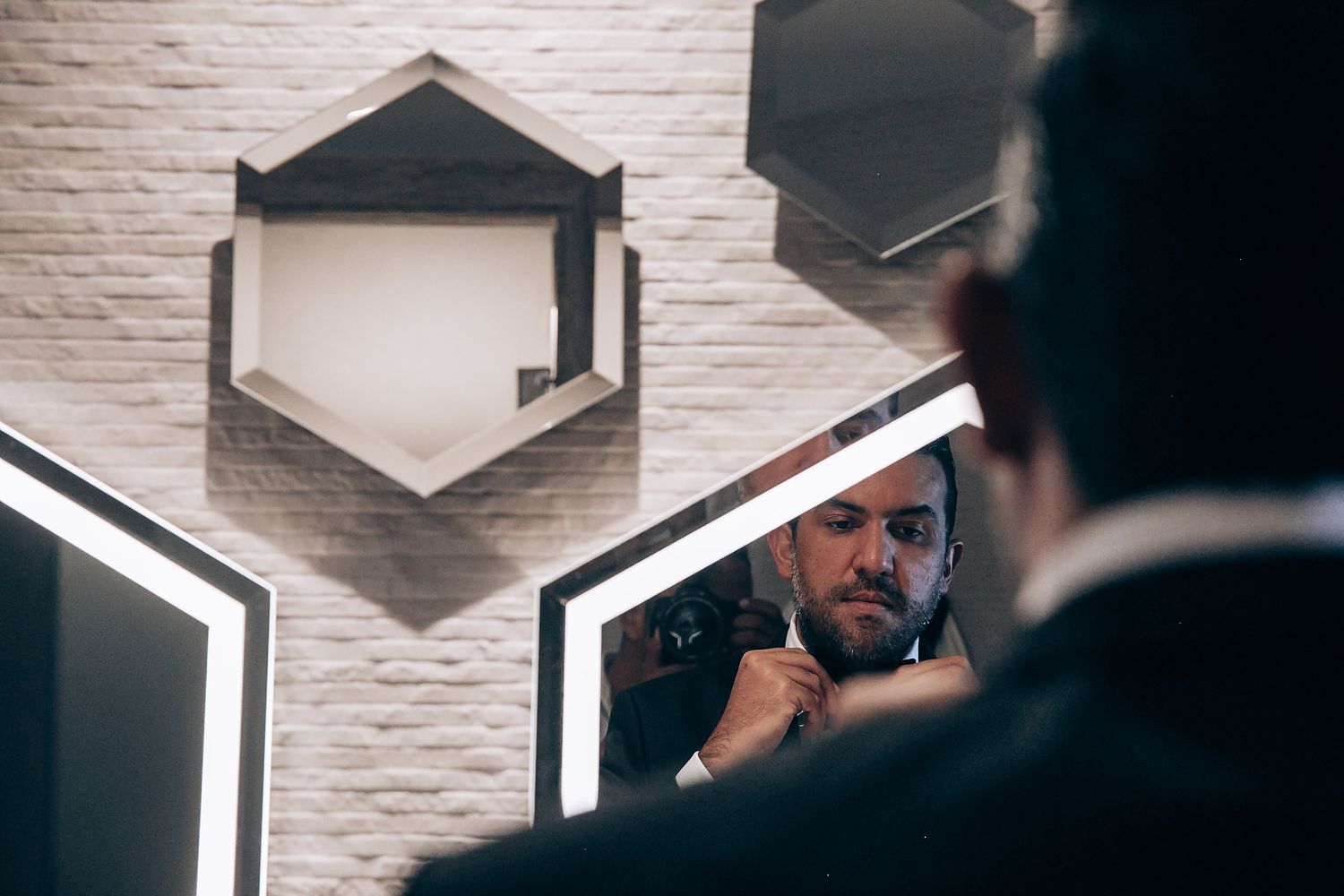 Professional barber uses scissors and comb while styling client's hair in modern barbershop with white brick walls.