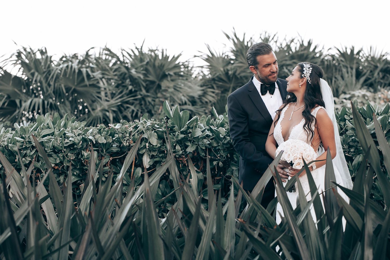 A romantic wedding moment captured among tropical foliage and greenery.