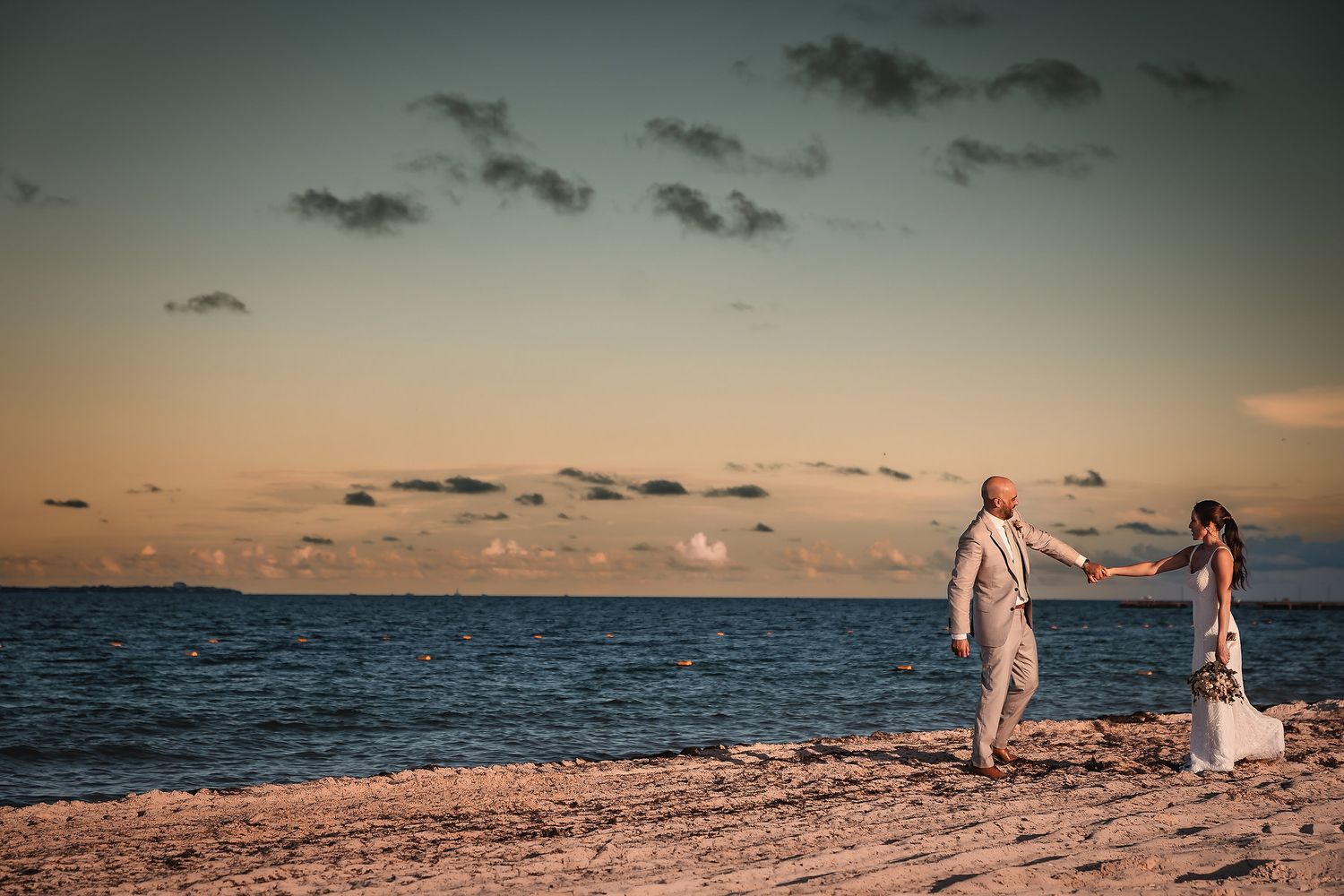 Silhouettes of a couple walking along a beach at dusk with a dramatic cloudy sky overhead.