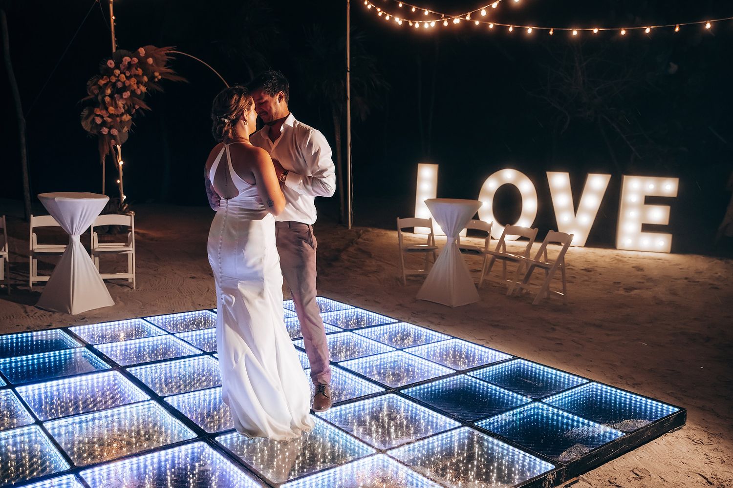 Wedding couple dancing on an illuminated LED dance floor with string lights overhead.