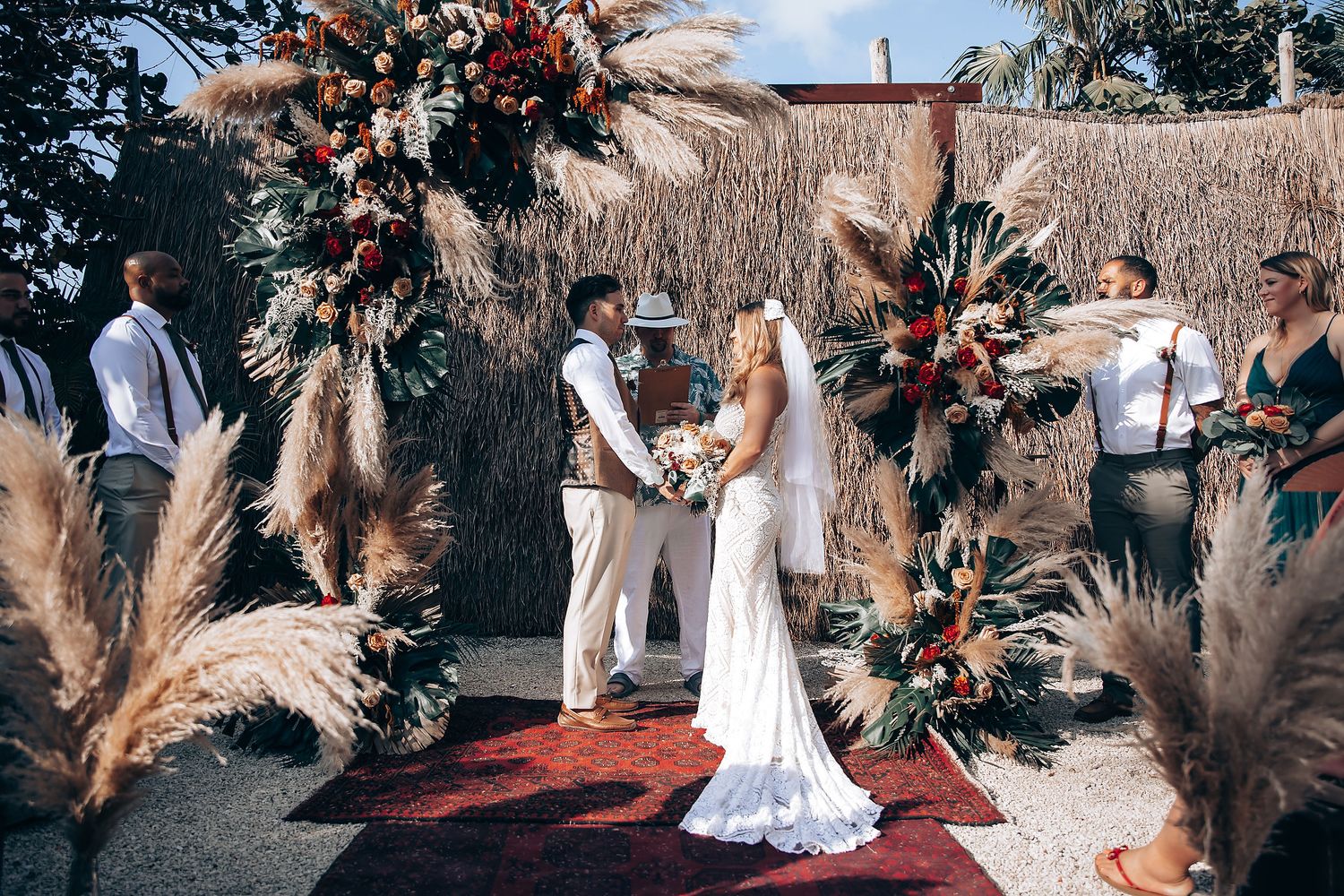 Wedding ceremony under palm trees with rustic boho decor and dried floral arrangements.