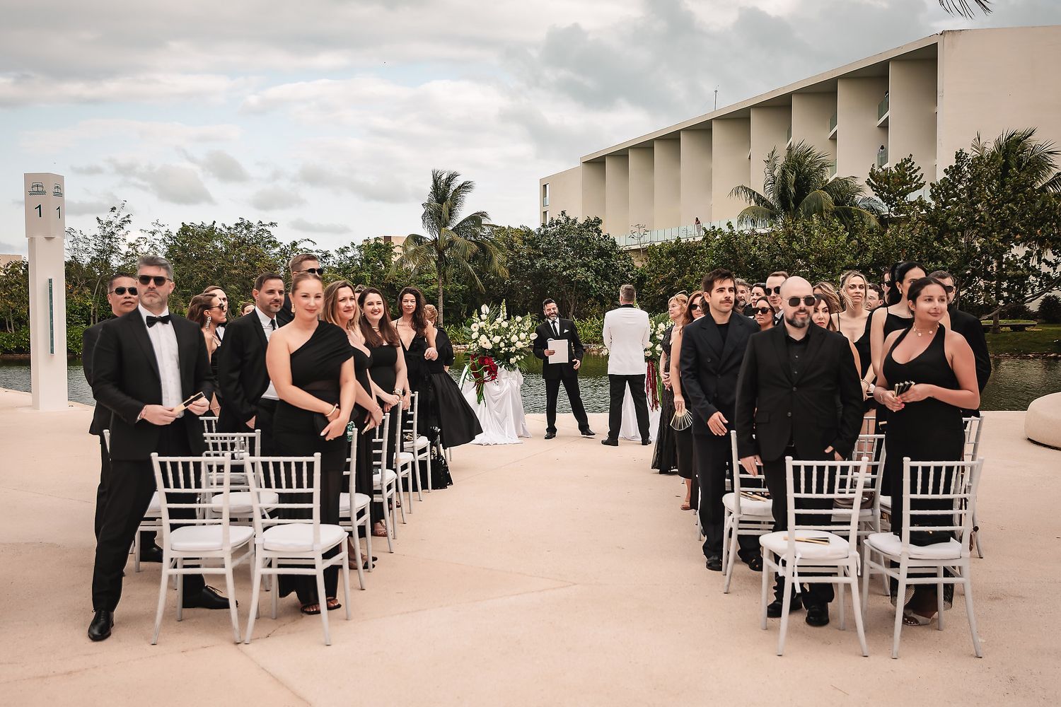 Wedding ceremony seating arrangement with white chairs and floral decorations in an outdoor setting.