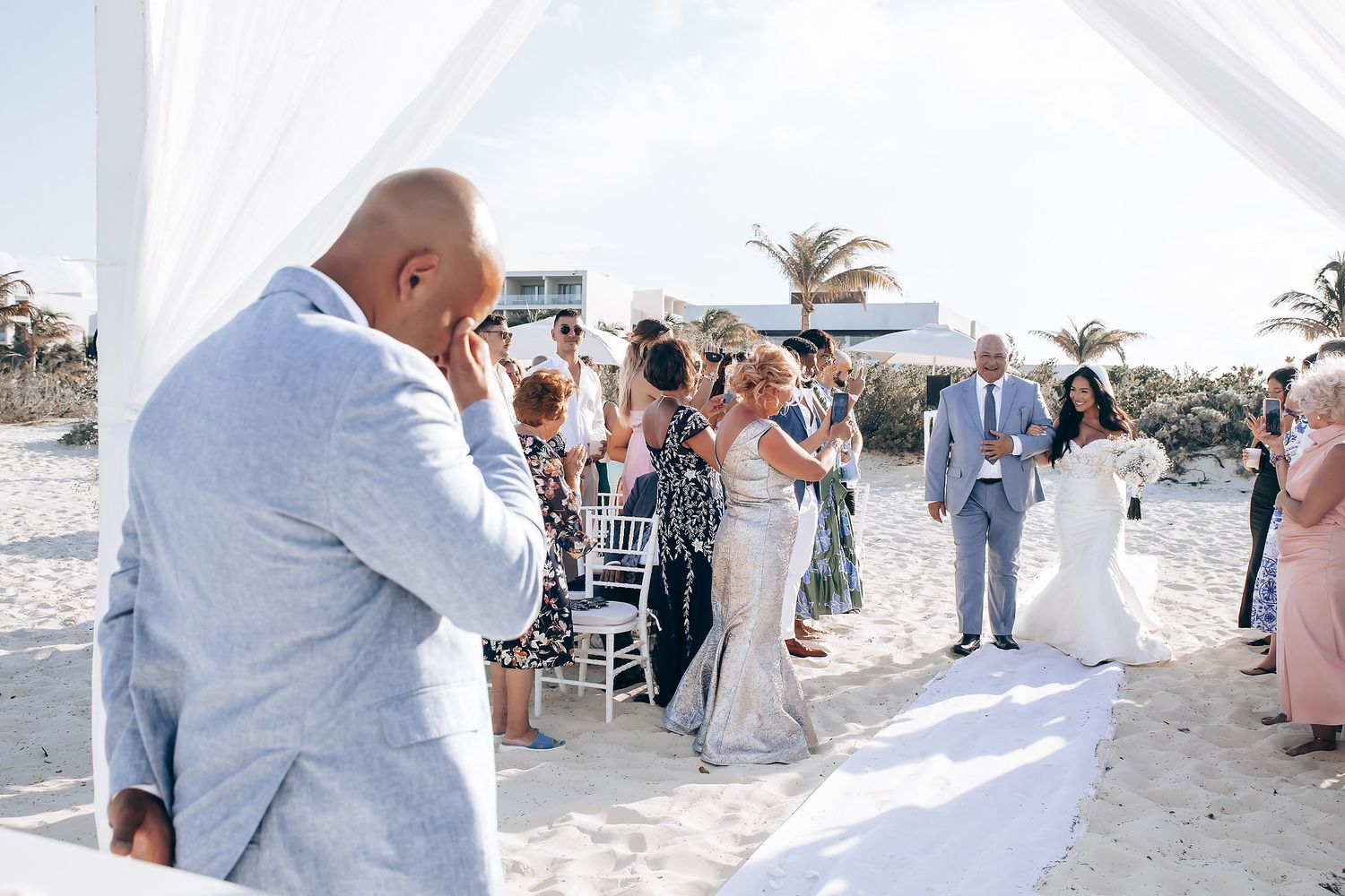 Wedding couple sharing a joyful moment on a sunny beach with palm trees in the background.