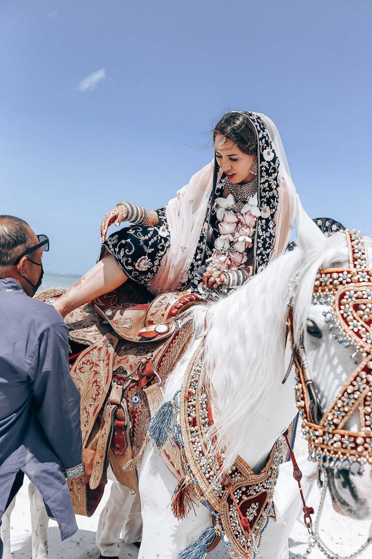 Person in ornate white dress and floral headscarf twirls on beach.