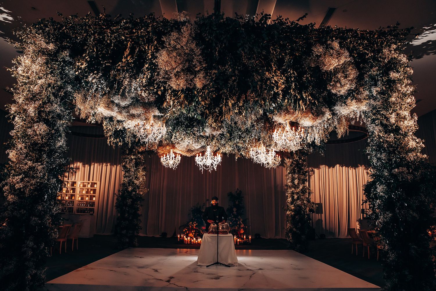 Wedding reception venue with dramatic lighting and hanging floral installations.