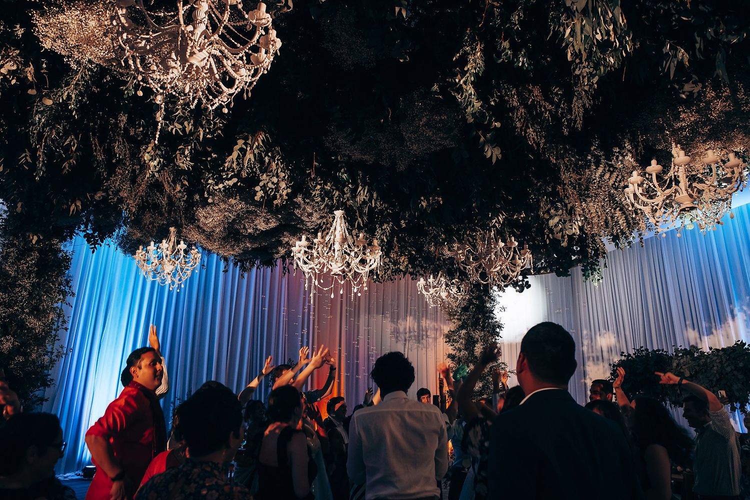 Silhouetted wedding guests dancing beneath chandeliers and decorative lighting.