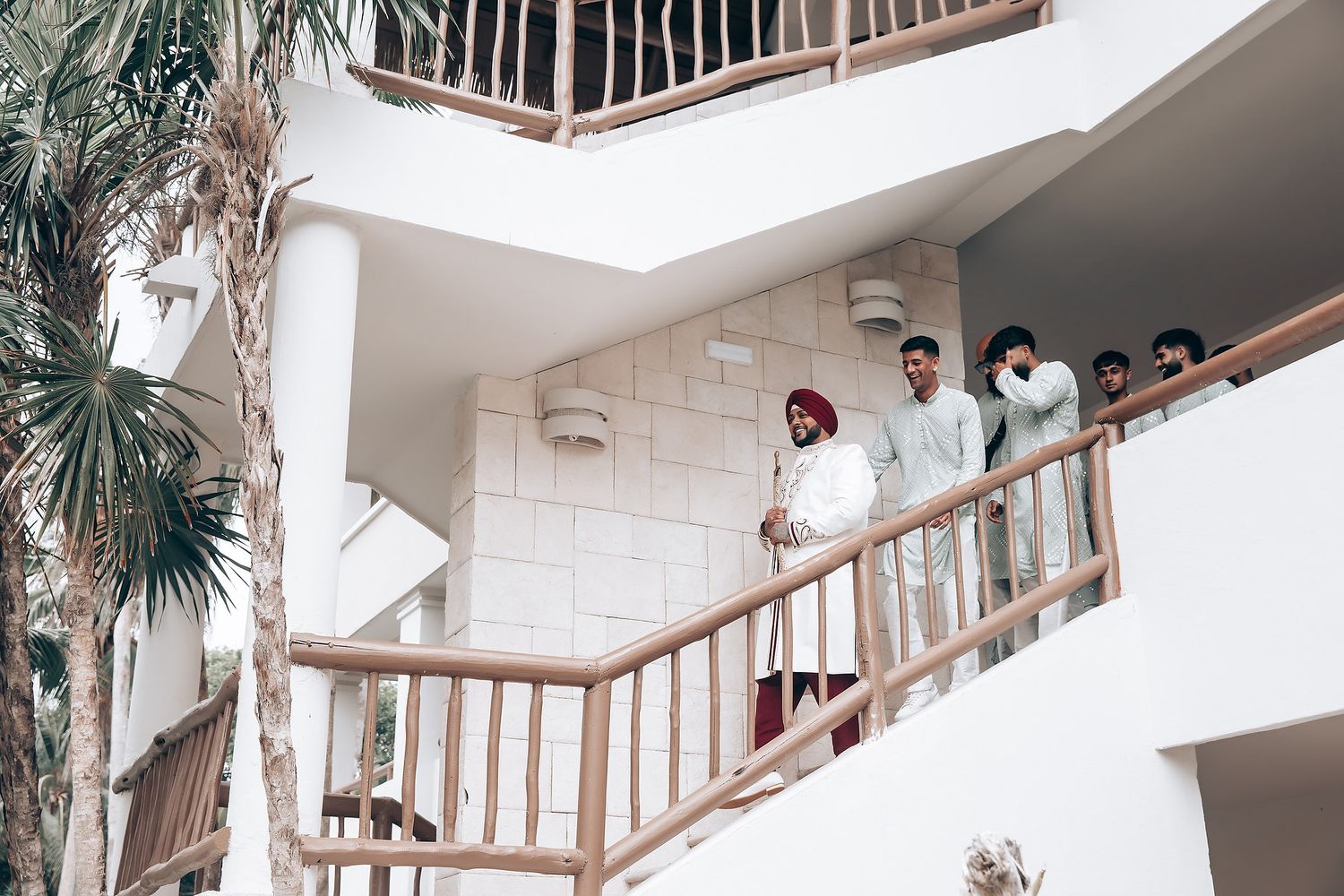 Wedding party members standing on a white balcony with palm trees in the background.