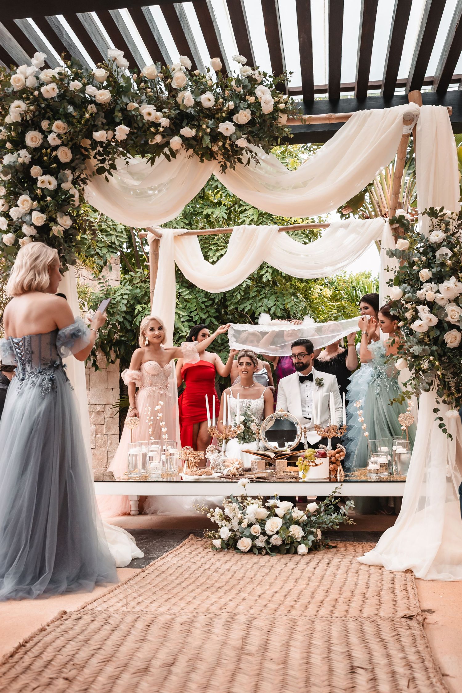 Wedding celebration under a pergola decorated with blush roses and flowing fabric.