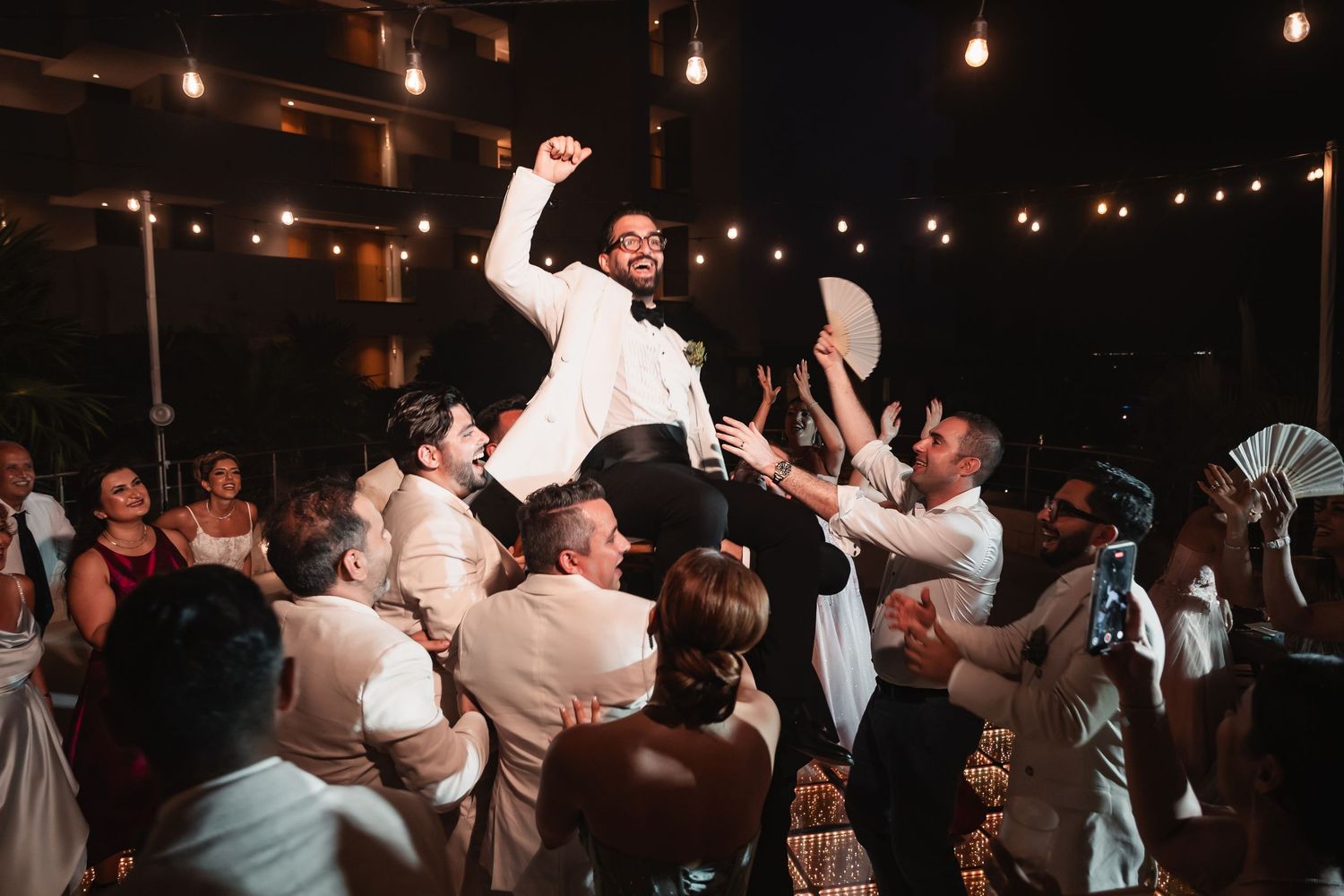 Party venue with hanging Edison bulbs creating ambient lighting over a crowded dance floor.