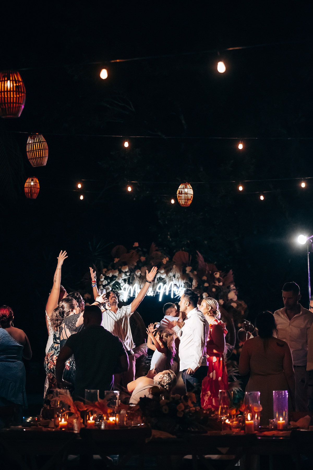 Nighttime wedding reception with hanging lanterns and string lights creating a magical atmosphere.