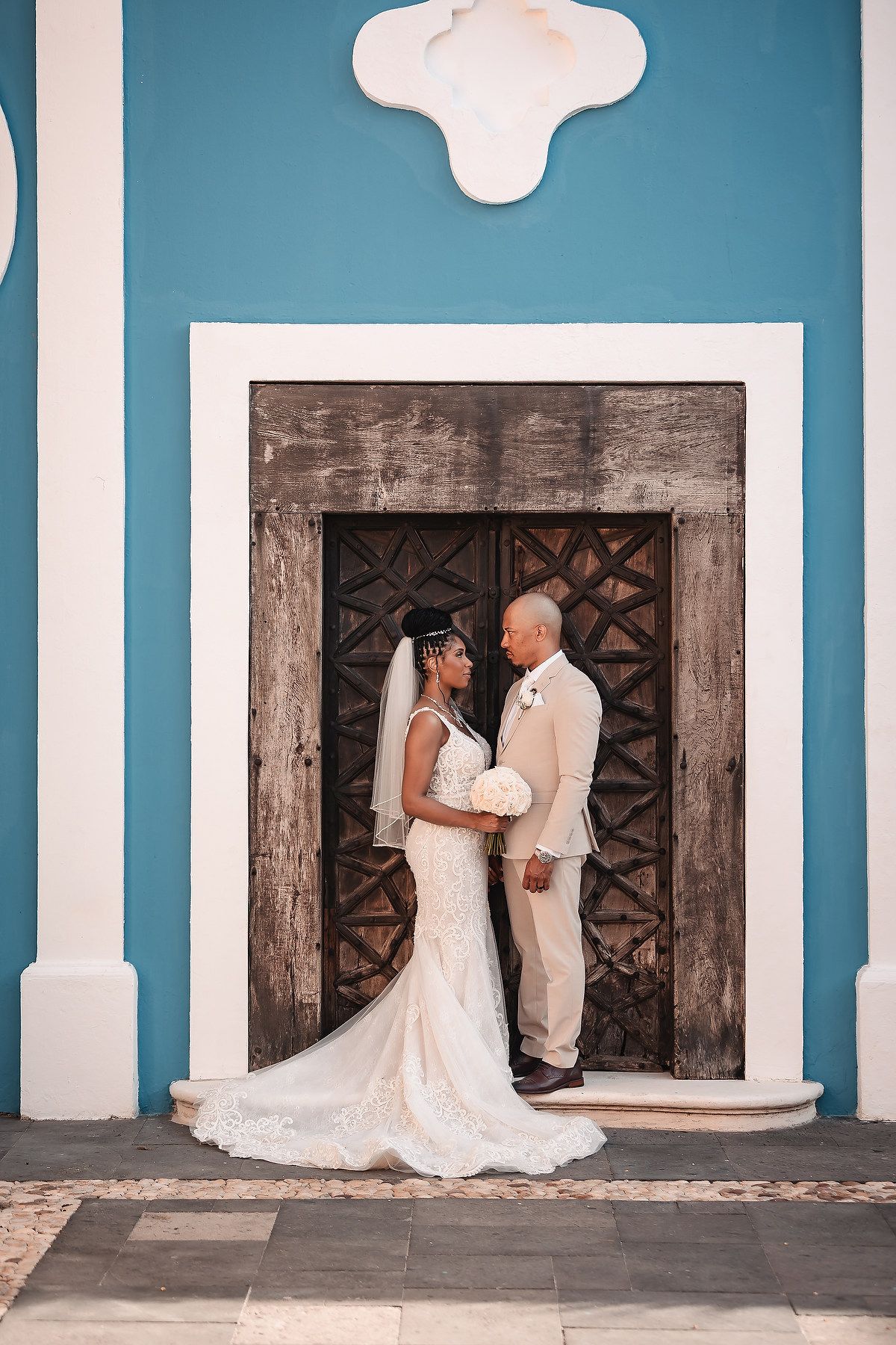 A wedding portrait in front of a turquoise wall and vintage wooden door with architectural details.
