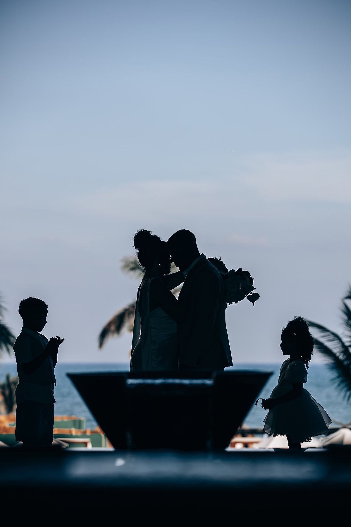 Silhouettes of people against a blue sky with palm trees at sunset.