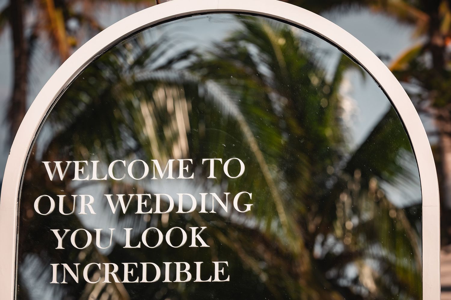 Welcome sign for a beach wedding with palm trees and ocean in background.