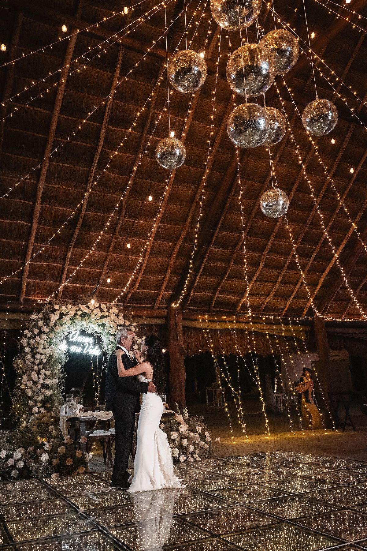 A couple shares their first dance in a rustic barn venue decorated with twinkling lights and disco balls.