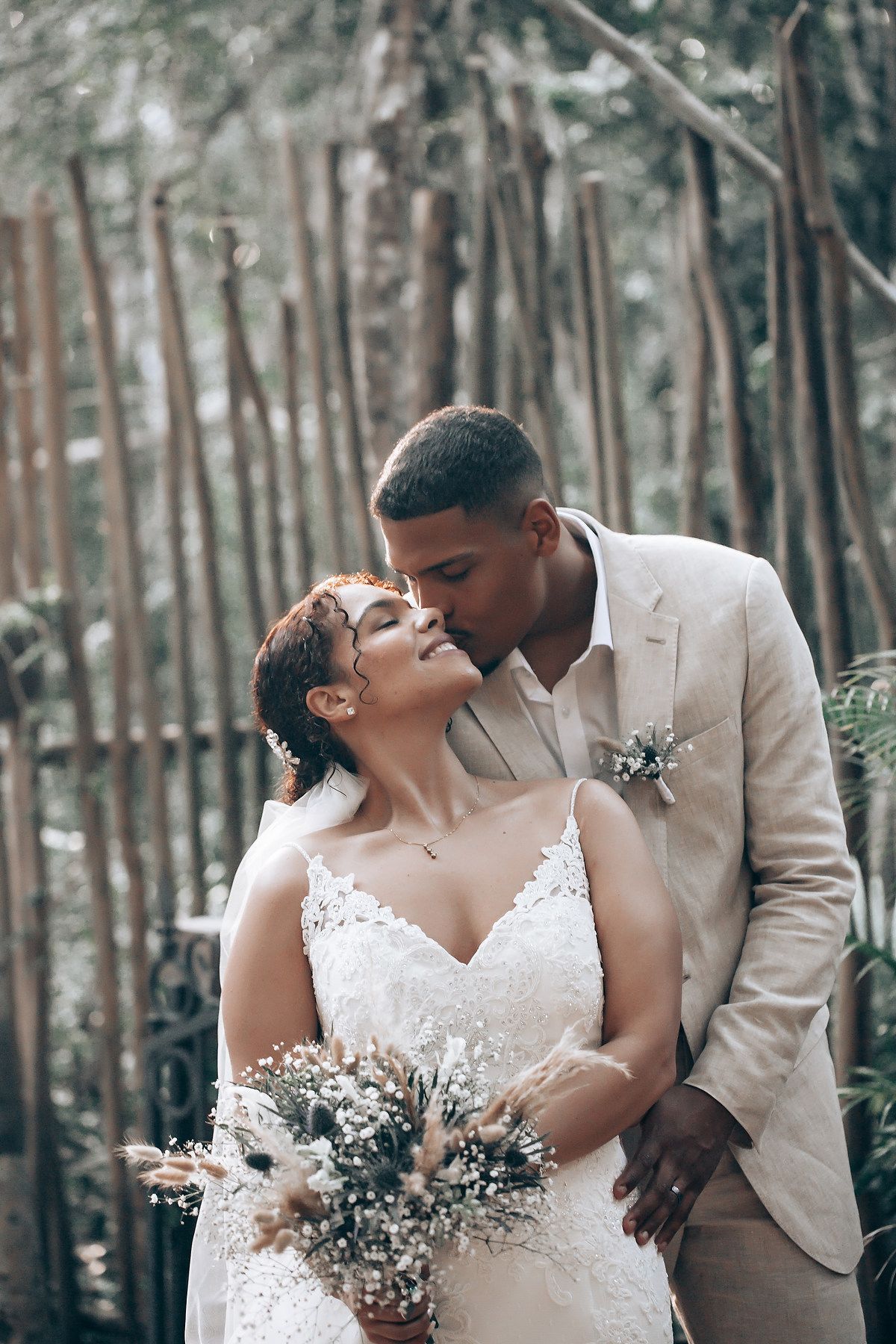 Romantic wedding couple shares intimate moments in a forest setting with soft lighting and white floral bouquet.