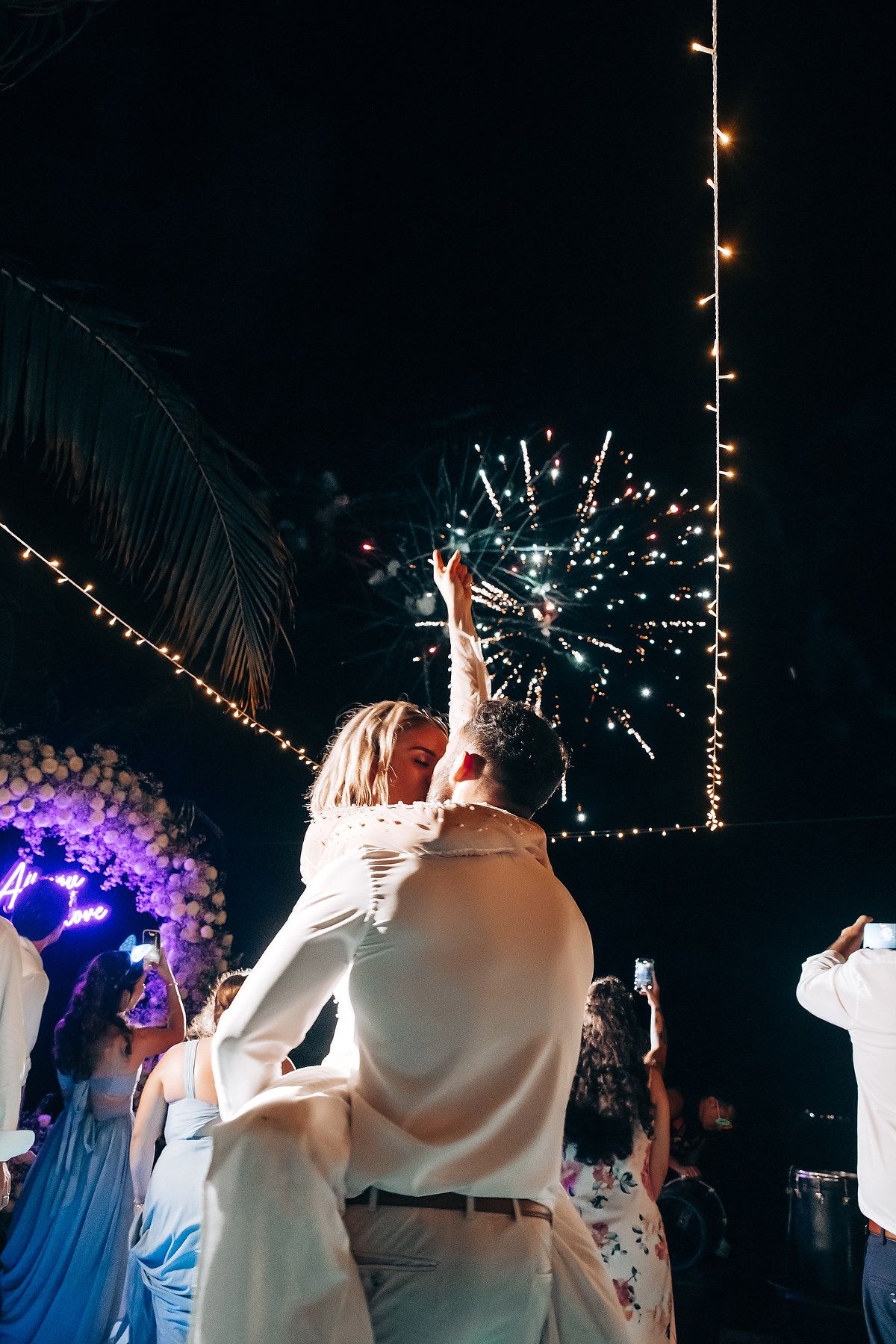 Wedding celebration at night with sparklers and string lights creating magical atmosphere.