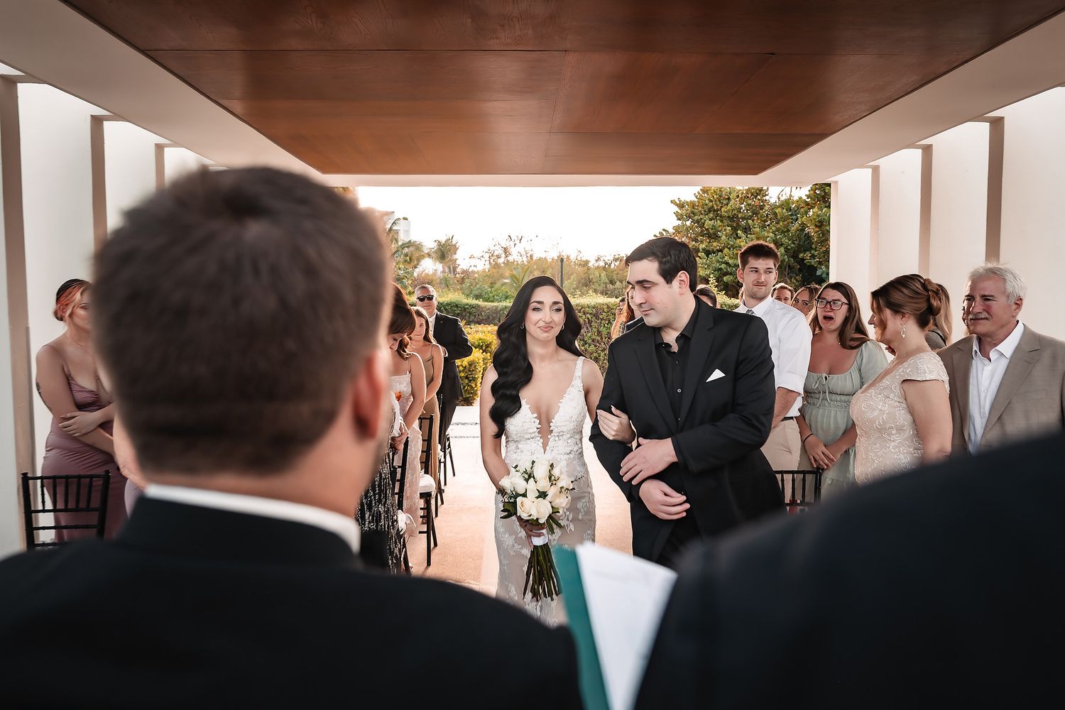 Outdoor wedding ceremony under covered walkway with tropical garden backdrop.