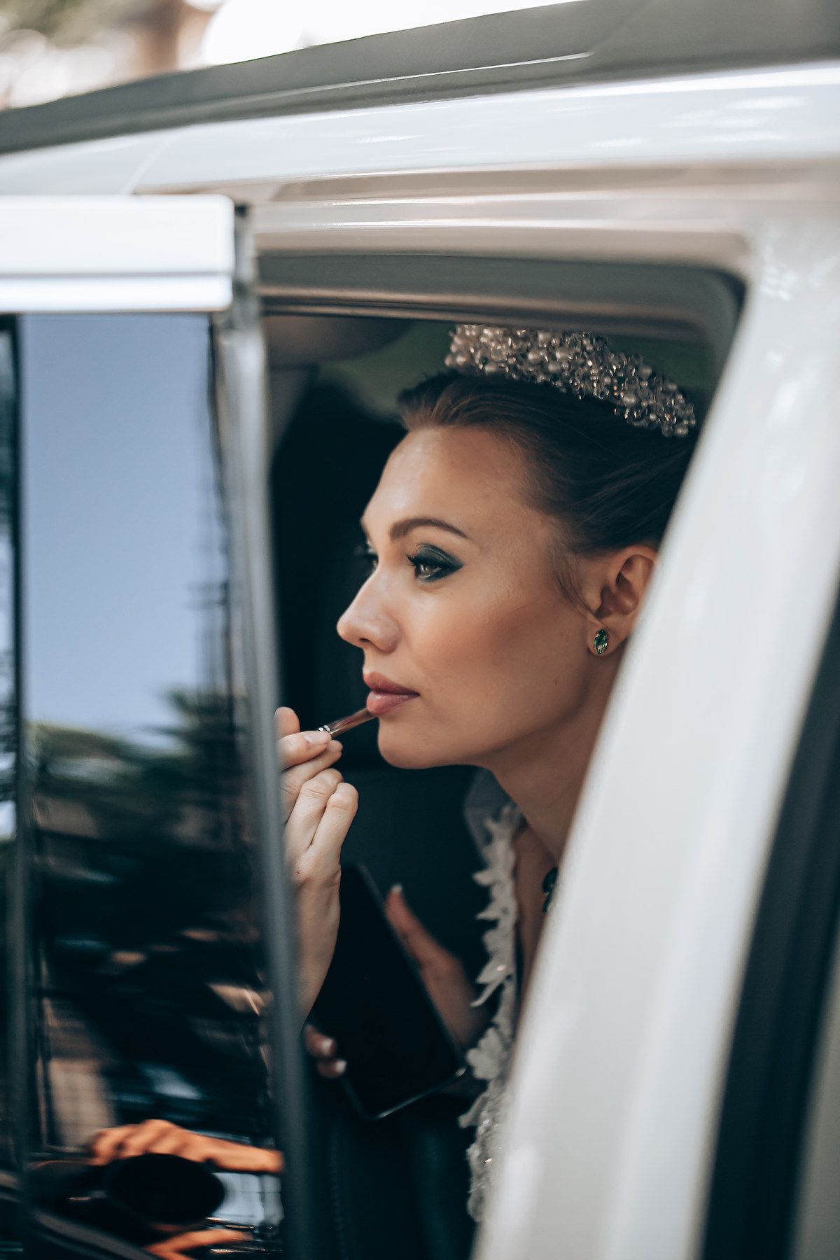 Close-up profile view through car window showing elegant makeup application in natural lighting.