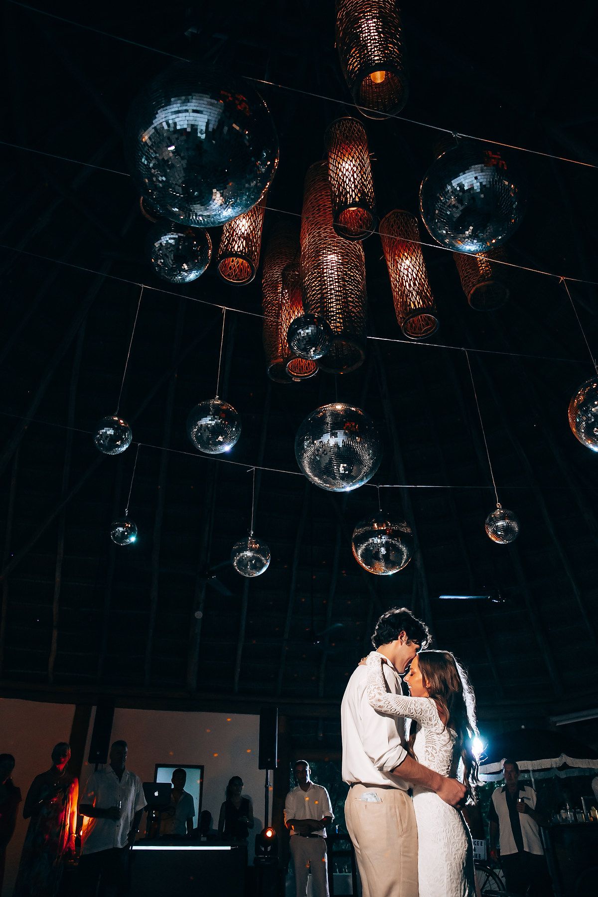 Couple shares their first dance under disco balls and ambient lighting at wedding reception.