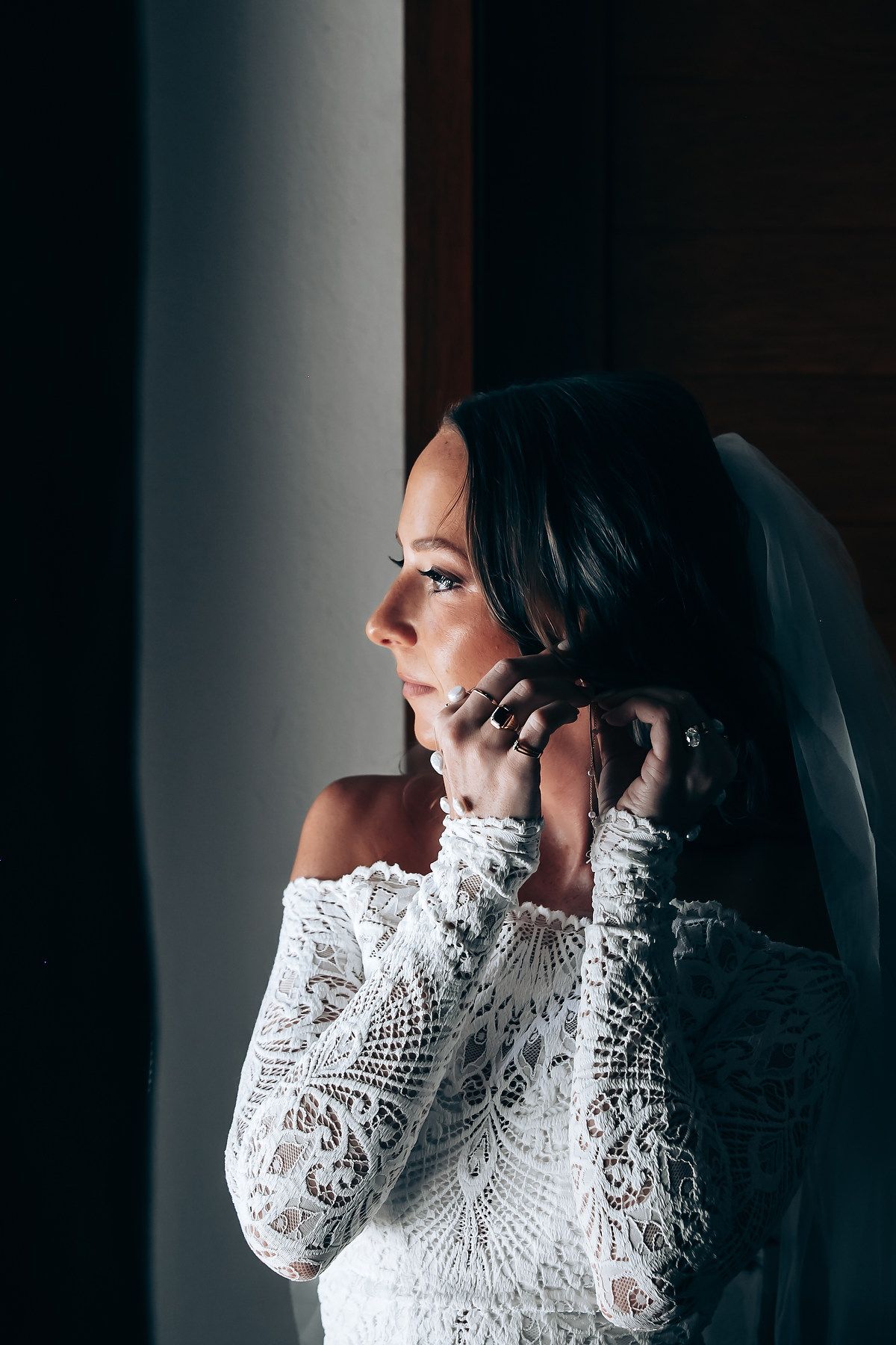 Elegant lace wedding dress with long sleeves photographed in dramatic window light.