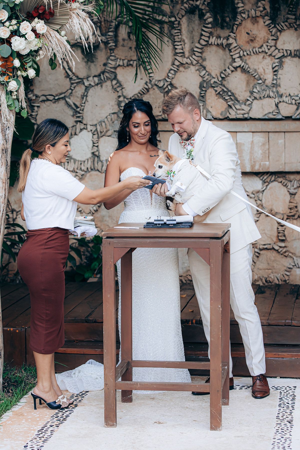 Wedding ceremony signing ritual at a wooden table against a decorative stone wall.