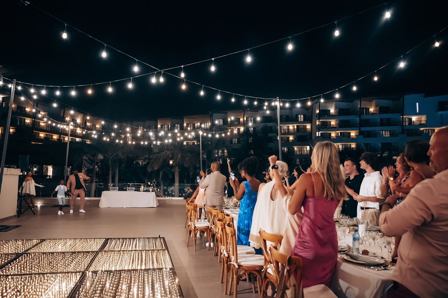 String lights illuminate an outdoor wedding reception area with rows of tables under the night sky.