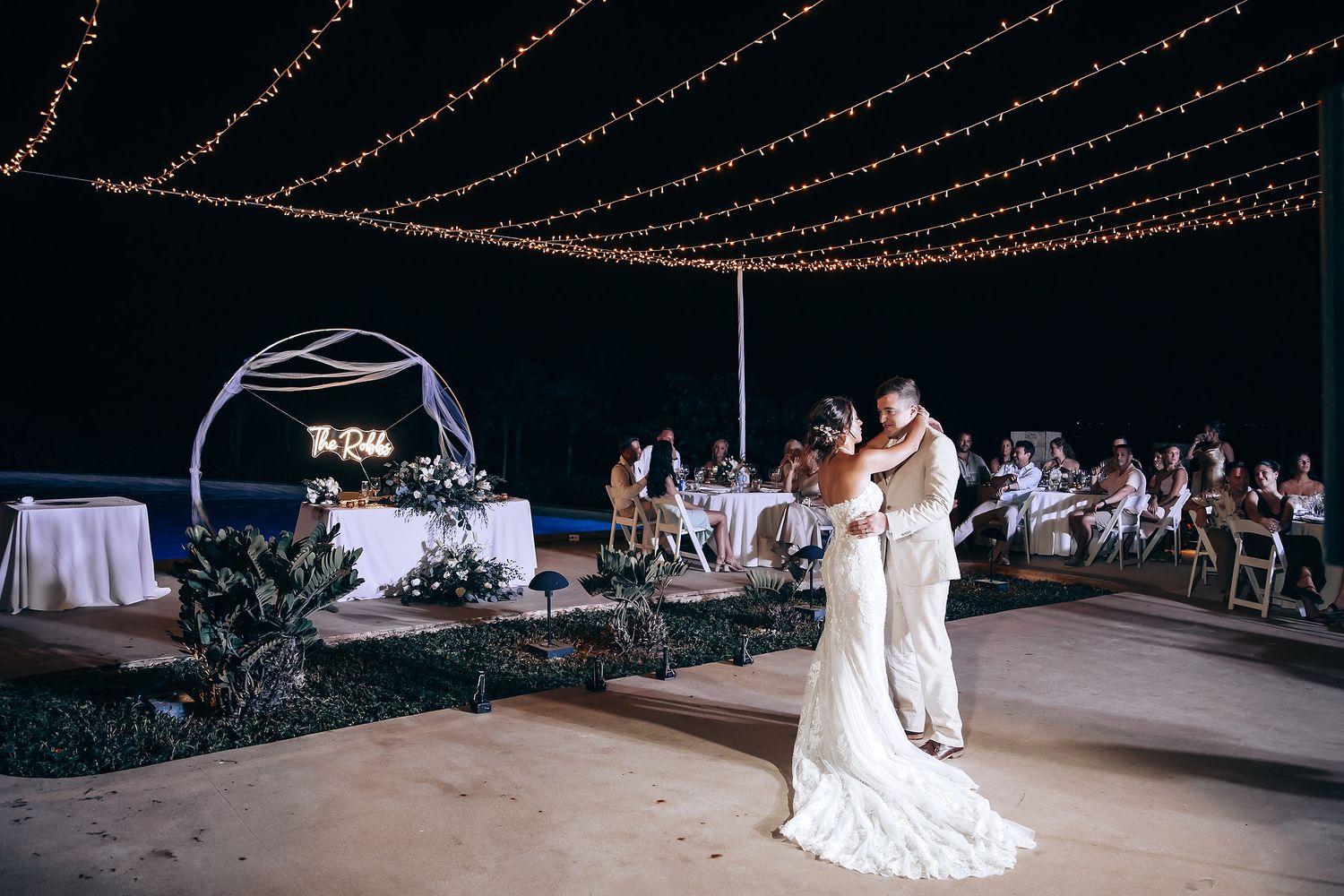Outdoor wedding reception venue decorated with romantic string lights and white linens.
