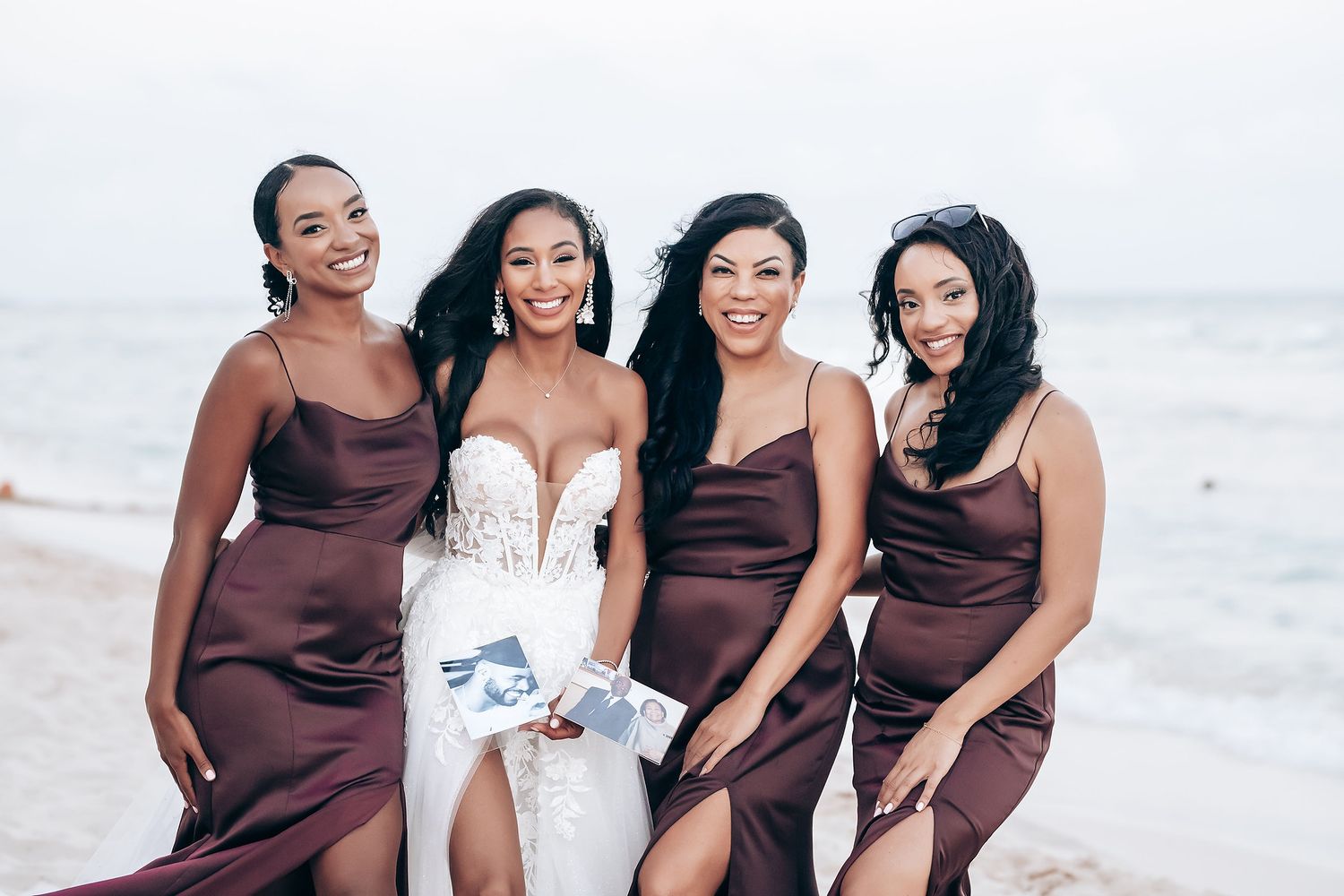 Bridal party in burgundy dresses posing together on a sunny beach.