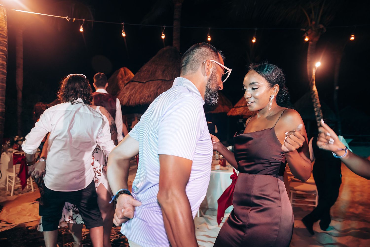 Wedding guests dancing together on a dimly lit dance floor with string lights overhead.