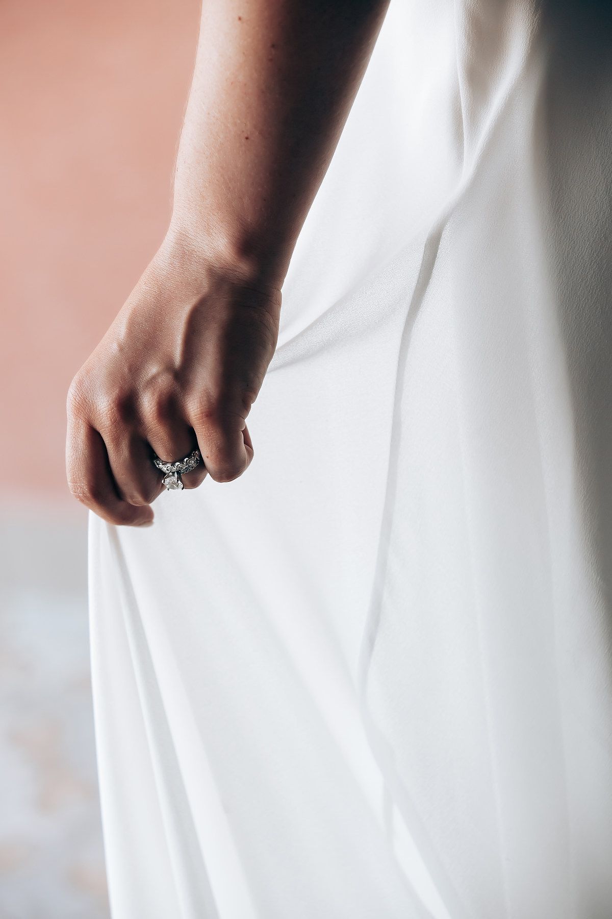 Elegant white wedding dress details and engagement ring captured in soft natural light.