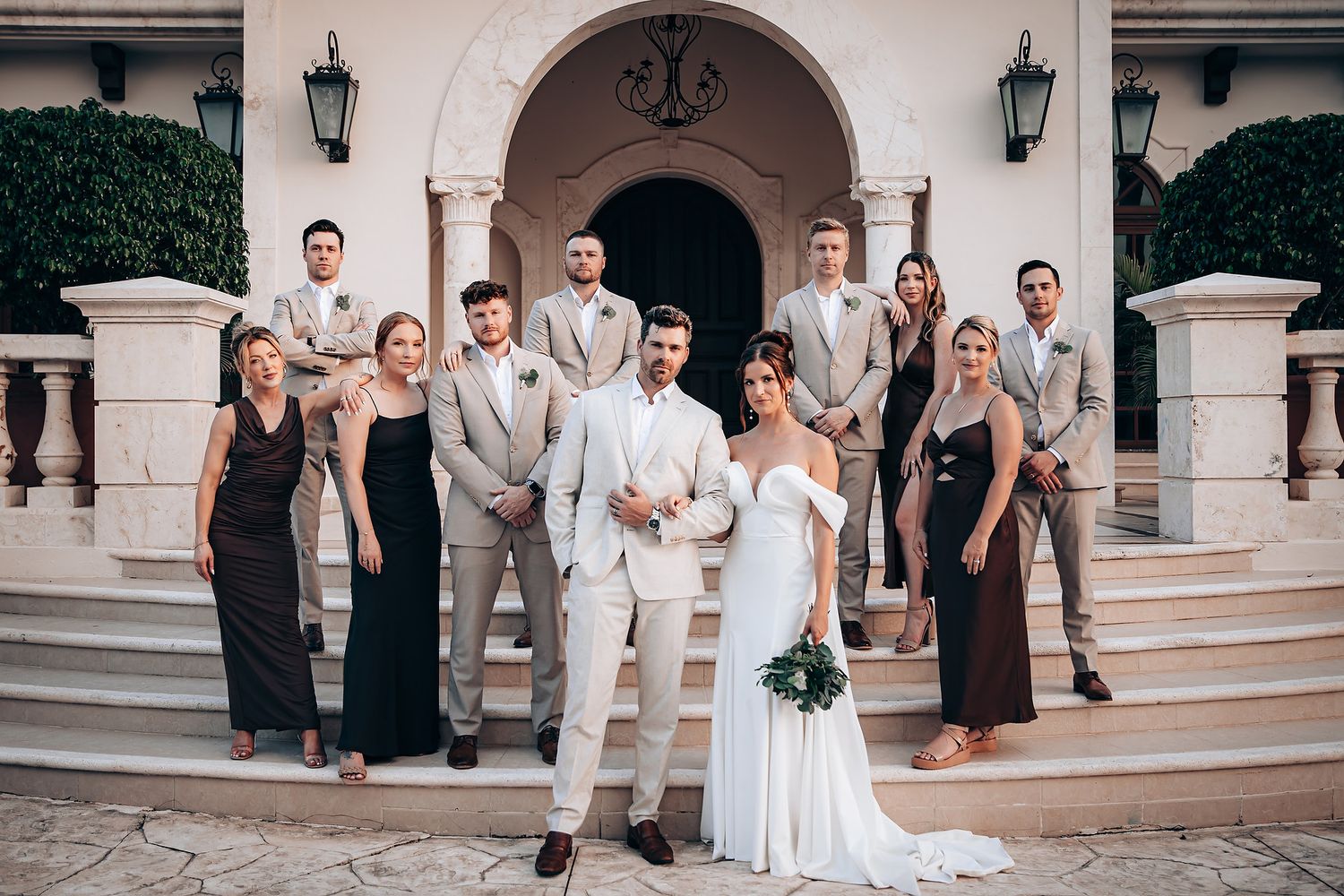 Wedding party group photos taken outside a classic white stucco building with arched entryways.
