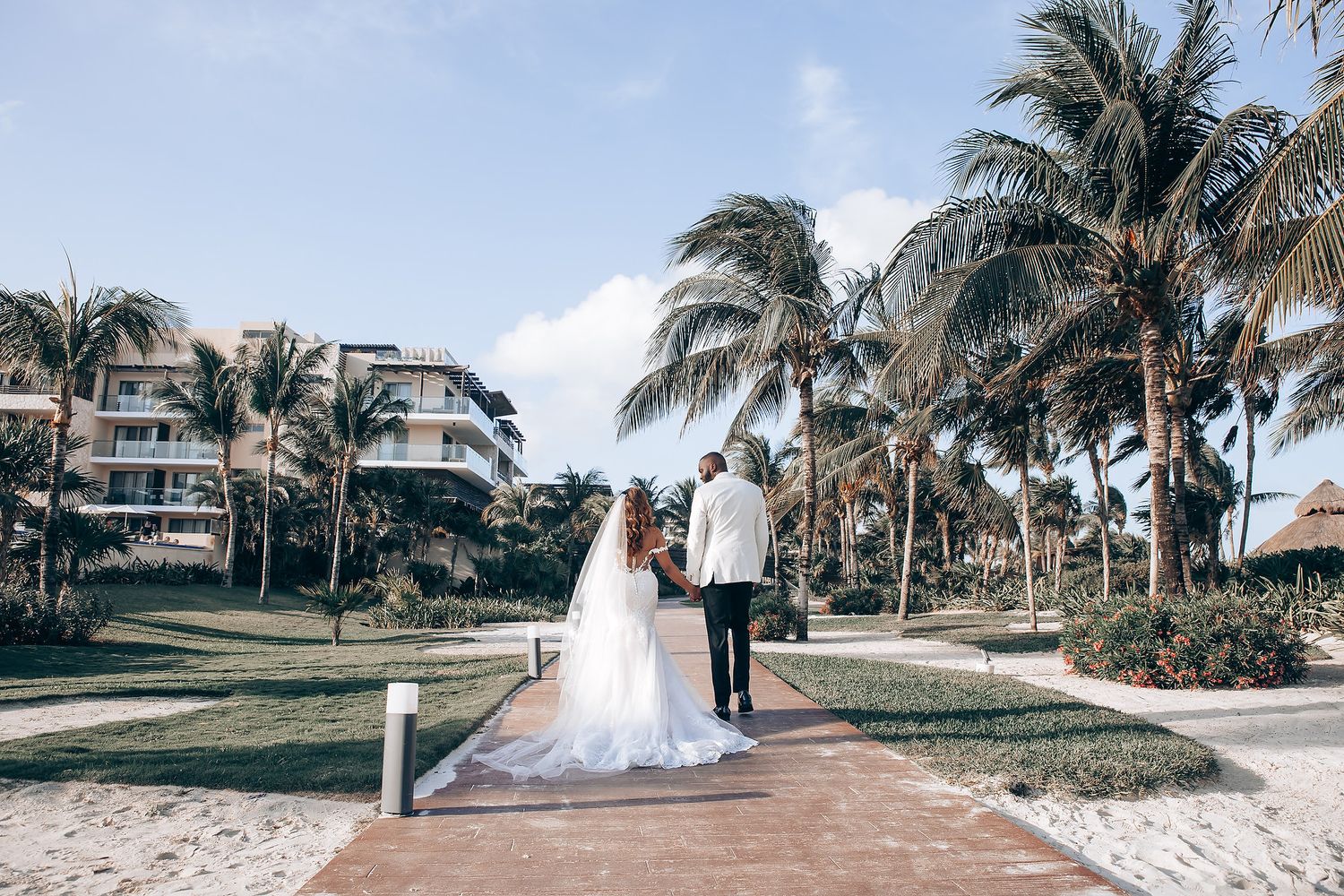 Palm trees line a beachfront wedding ceremony setup with white chairs and tropical scenery.