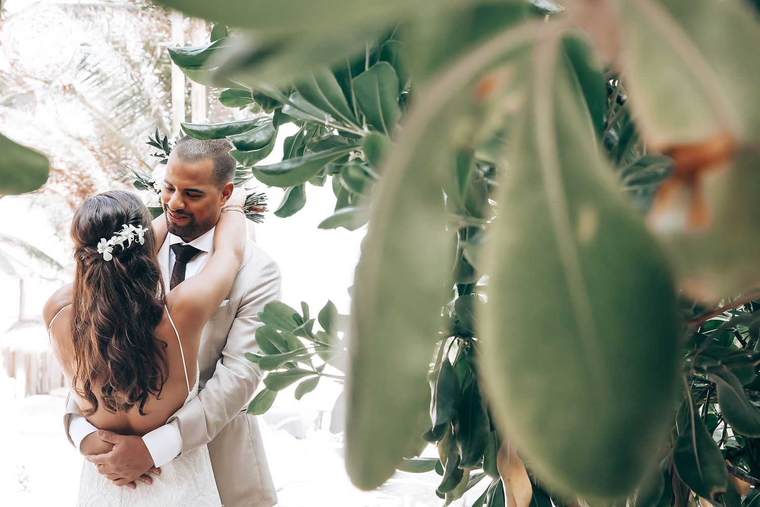 Intimate wedding photography through green foliage at a beach resort.