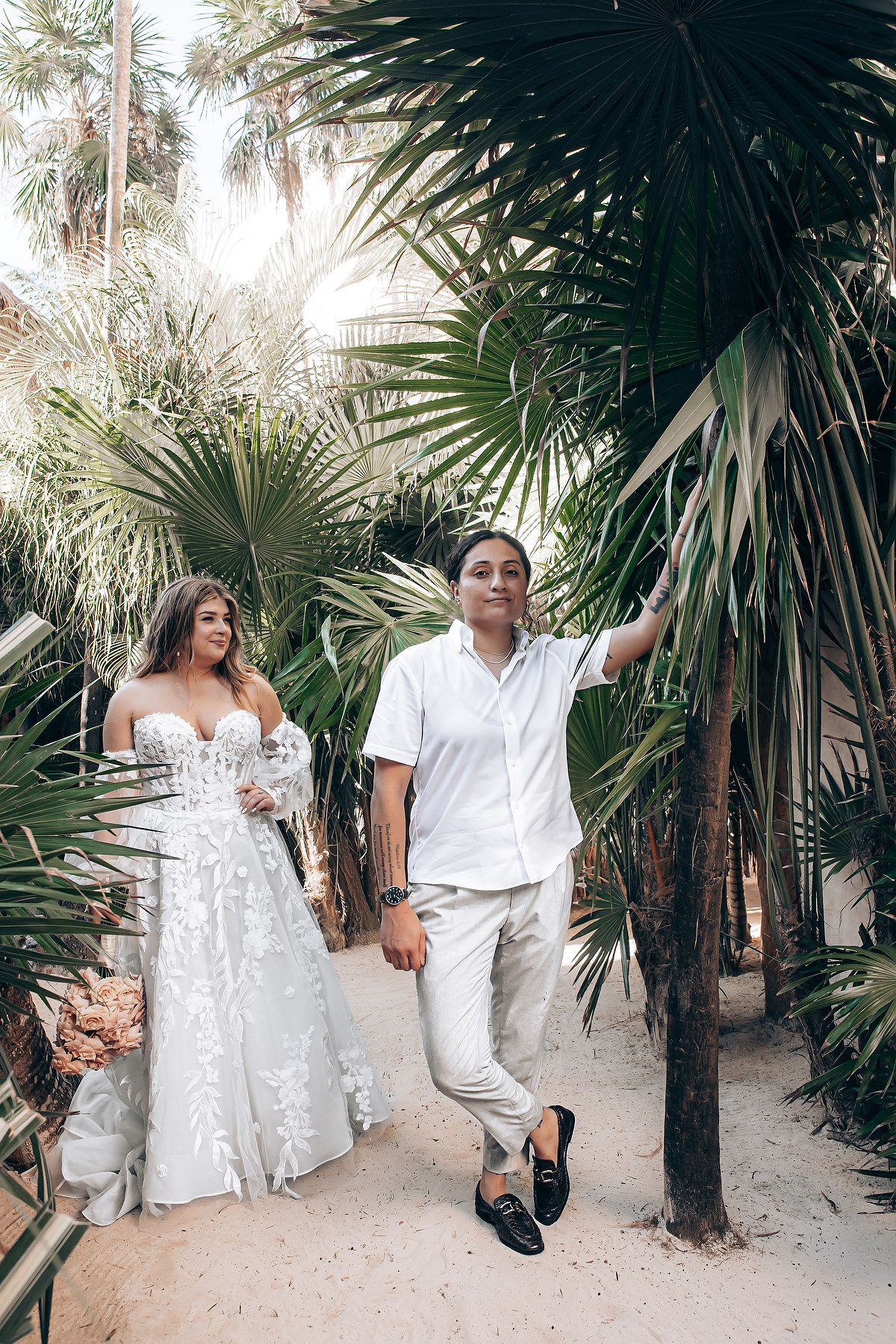 A couple poses among tropical palm trees during their destination wedding photoshoot.