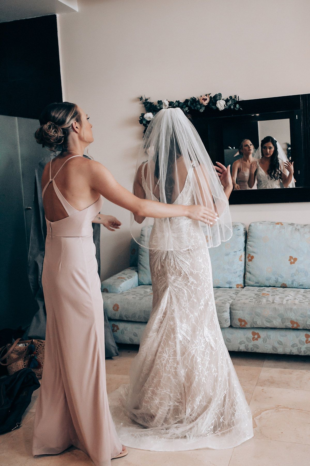 A touching moment between two people in a room, one wearing a pink dress and another in a white wedding gown with veil.