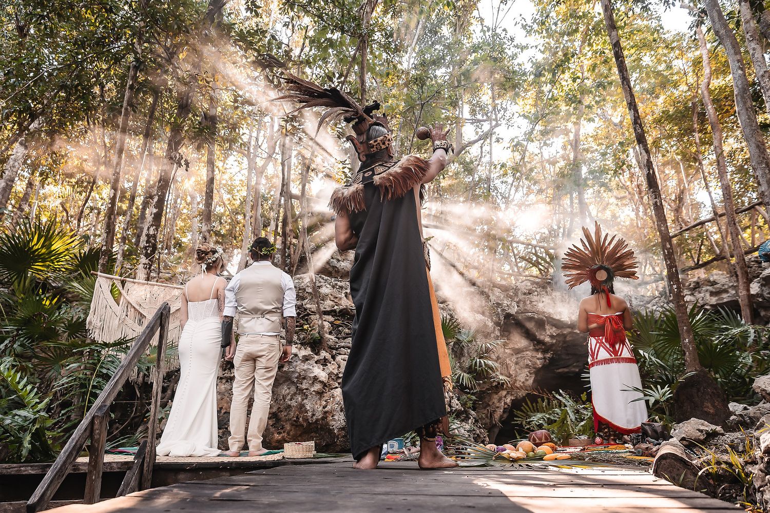 Mayan ceremony in a lush jungle setting with officiant in traditional headdress blessing a couple at their wedding.