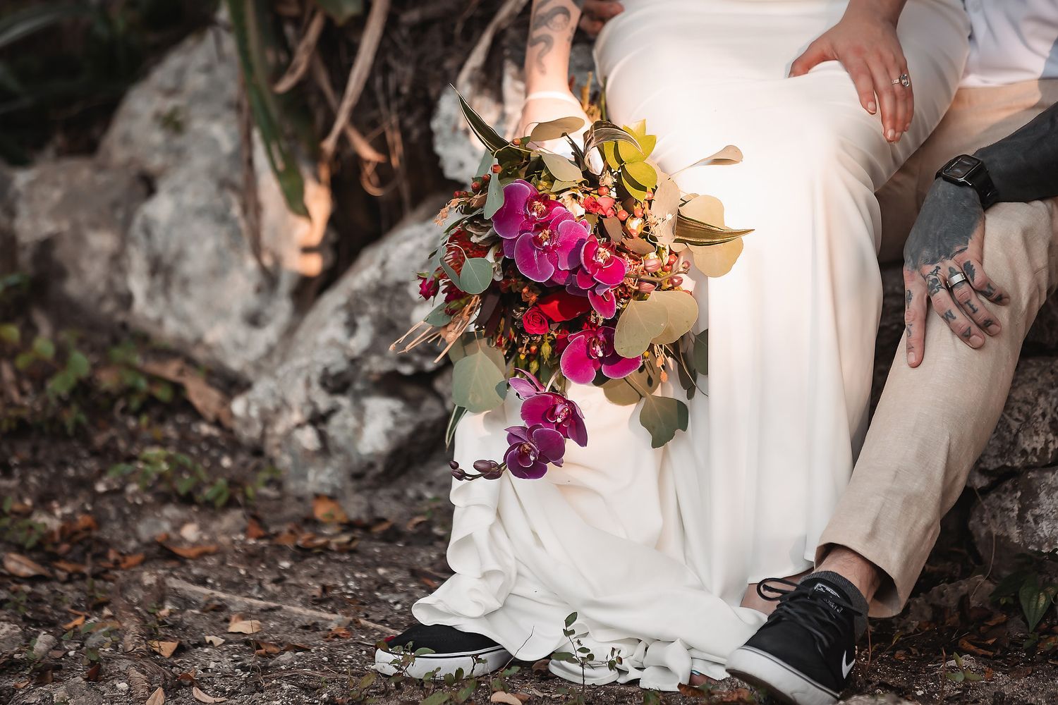 Close-up of a vibrant pink and purple bridal bouquet held by a bride in a white gown seated outdoors.