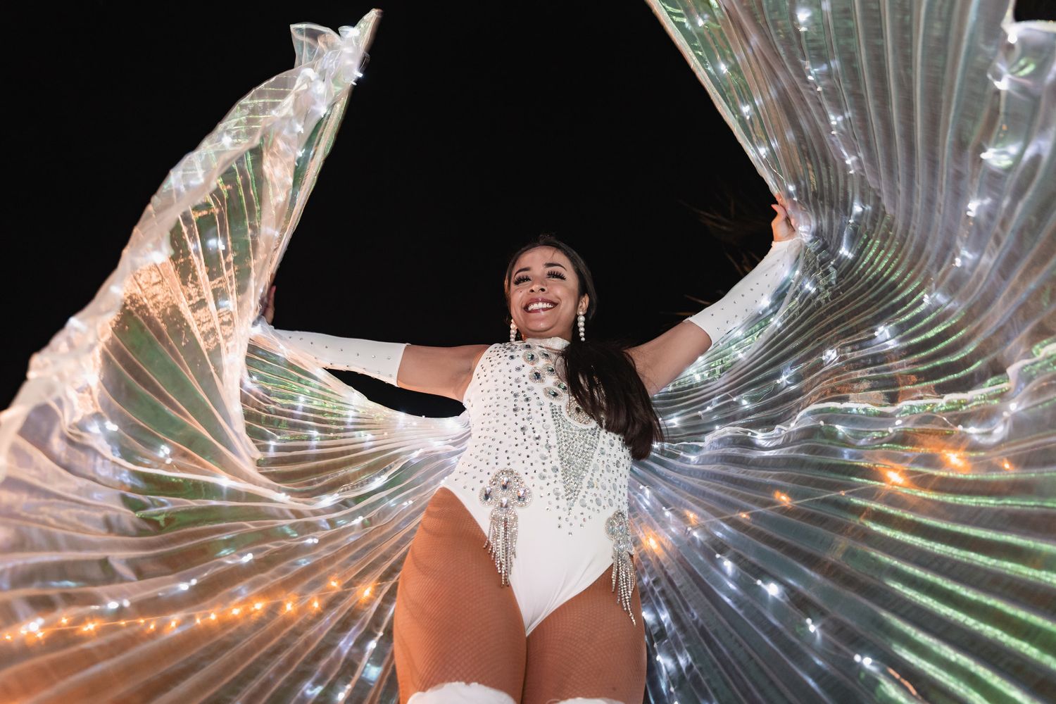 Performer in white sequined bodysuit with illuminated LED wings at wedding reception.