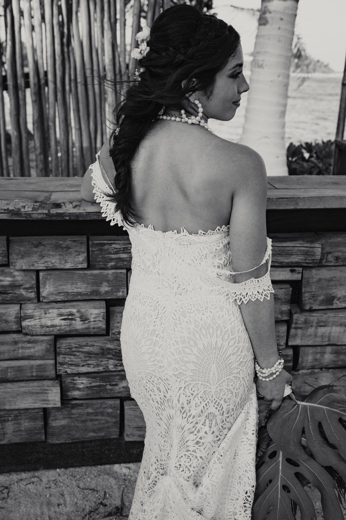 Black and white portrait of bride in lace off-shoulder gown with pearl jewelry at tropical venue.