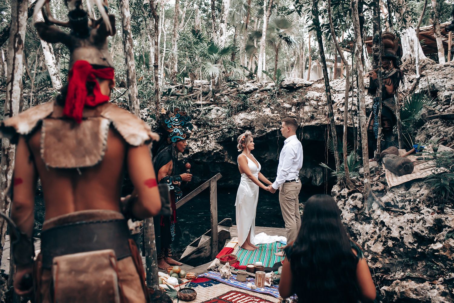 Outdoor gathering in a wooded area with people seated on blankets.