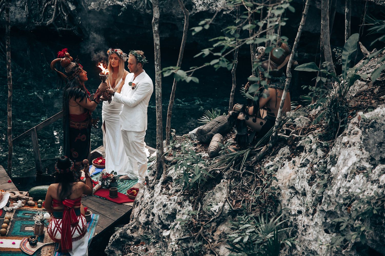 An intimate wedding ceremony takes place on a decorated platform in a tropical forest setting.