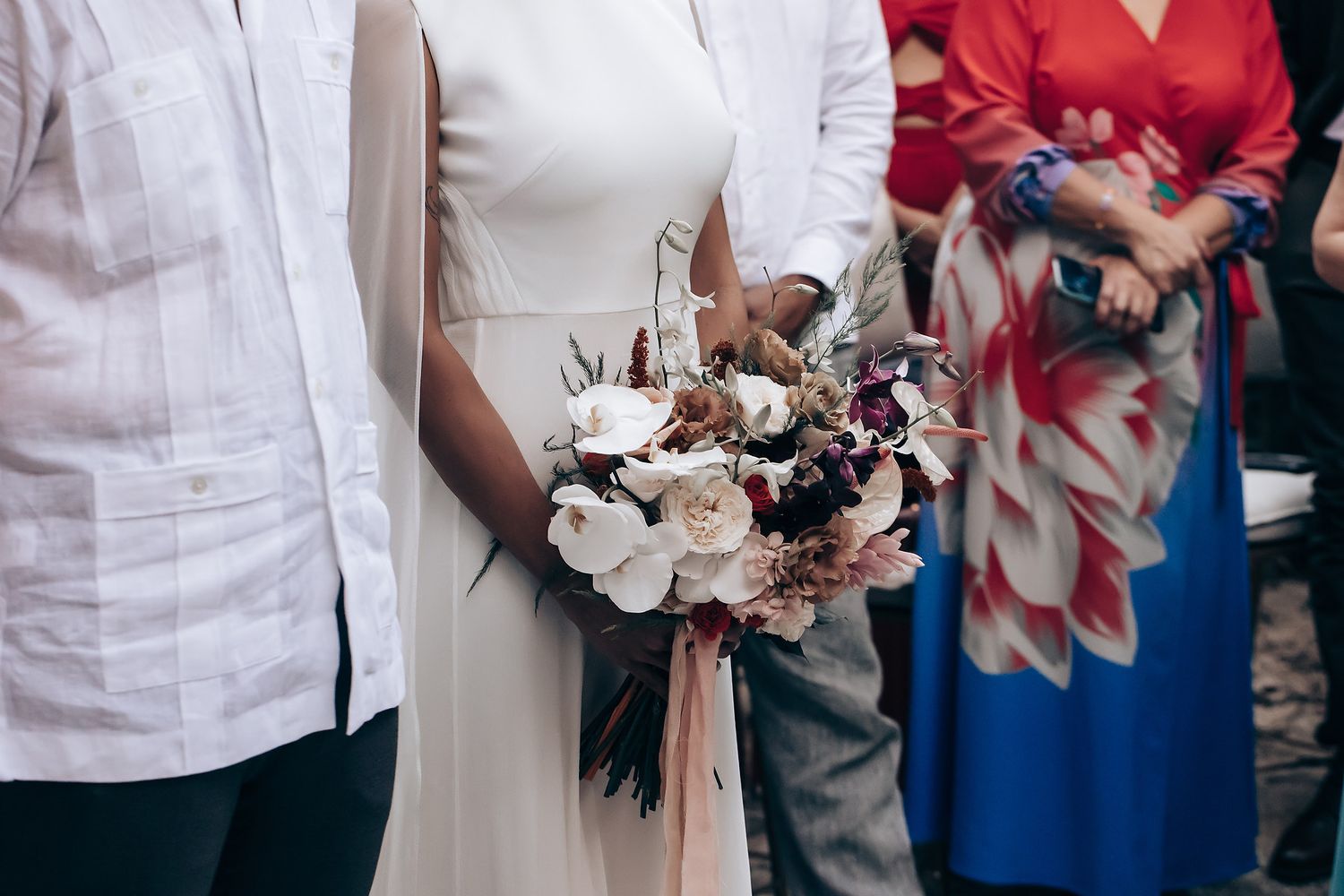 Wedding party members in white and red attire holding floral bouquets.
