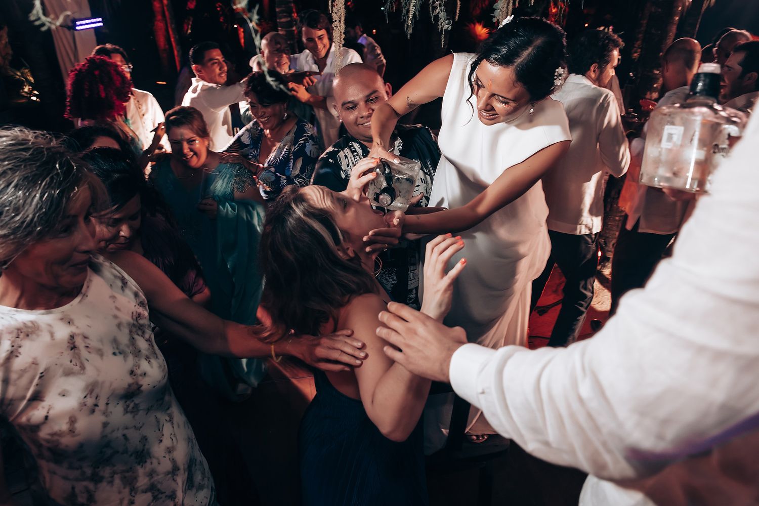 Crowded dance floor at a wedding reception with guests dancing under atmospheric lighting.