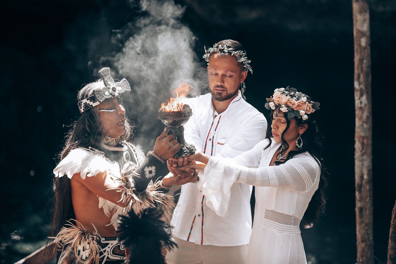 Smoke rises during a traditional spiritual ceremony as participants gather in white clothing.