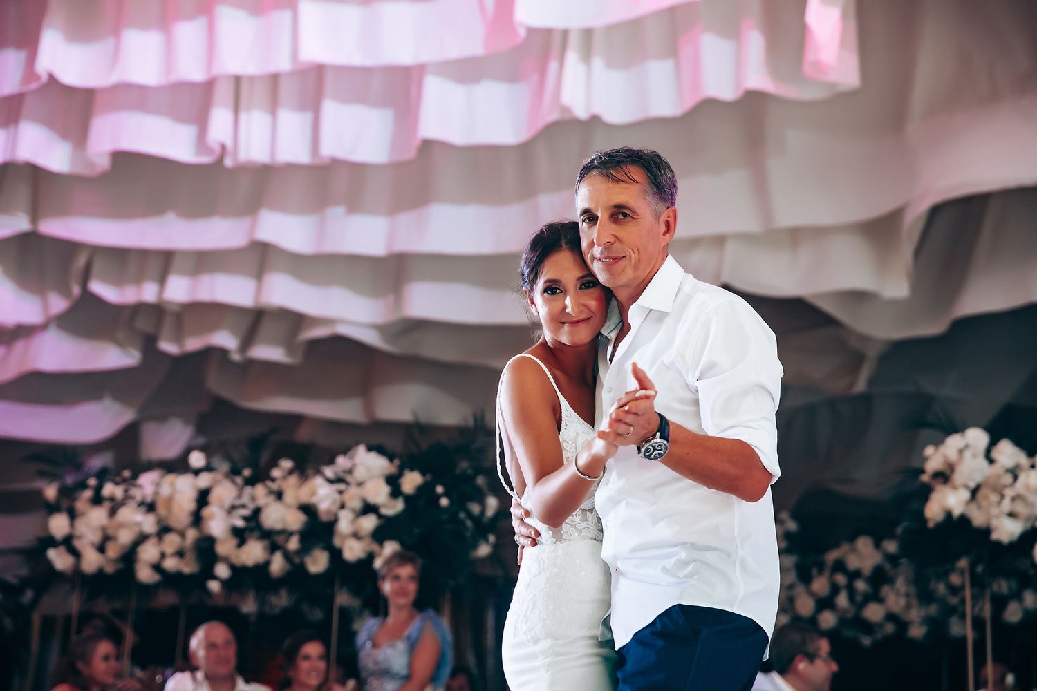 Wedding reception dance performance under elegant white draped ceiling with pink lighting.