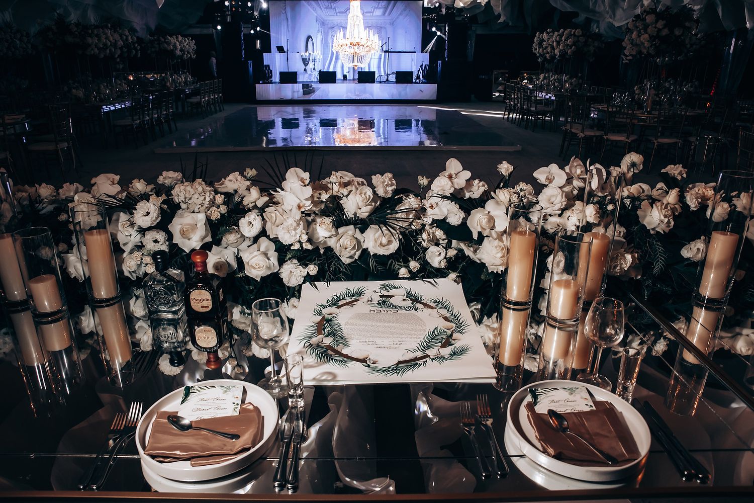 Dark reception venue decorated with abundant white floral arrangements and mood lighting.