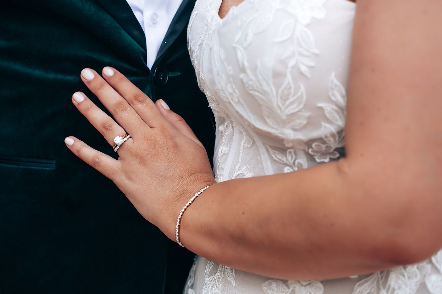 Detail shot of hands wearing wedding rings against white dress.